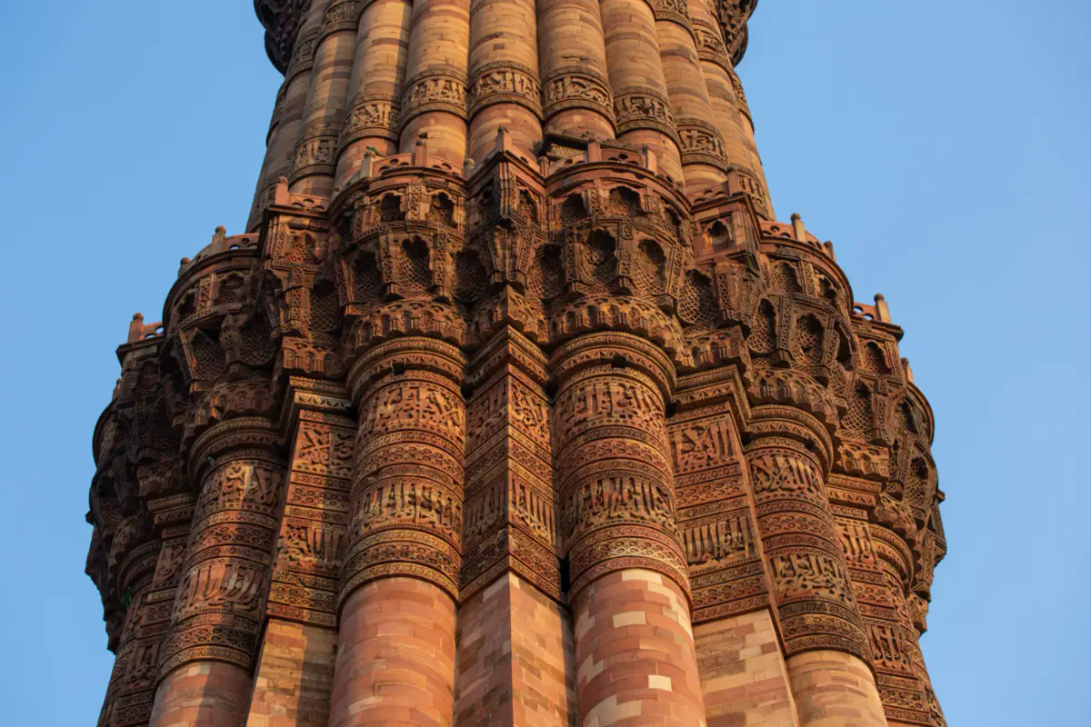 Close view of the Qutb Minar's fluted red sandstone shaft and a balcony, carved with bands of calligraphy, against a blue sky