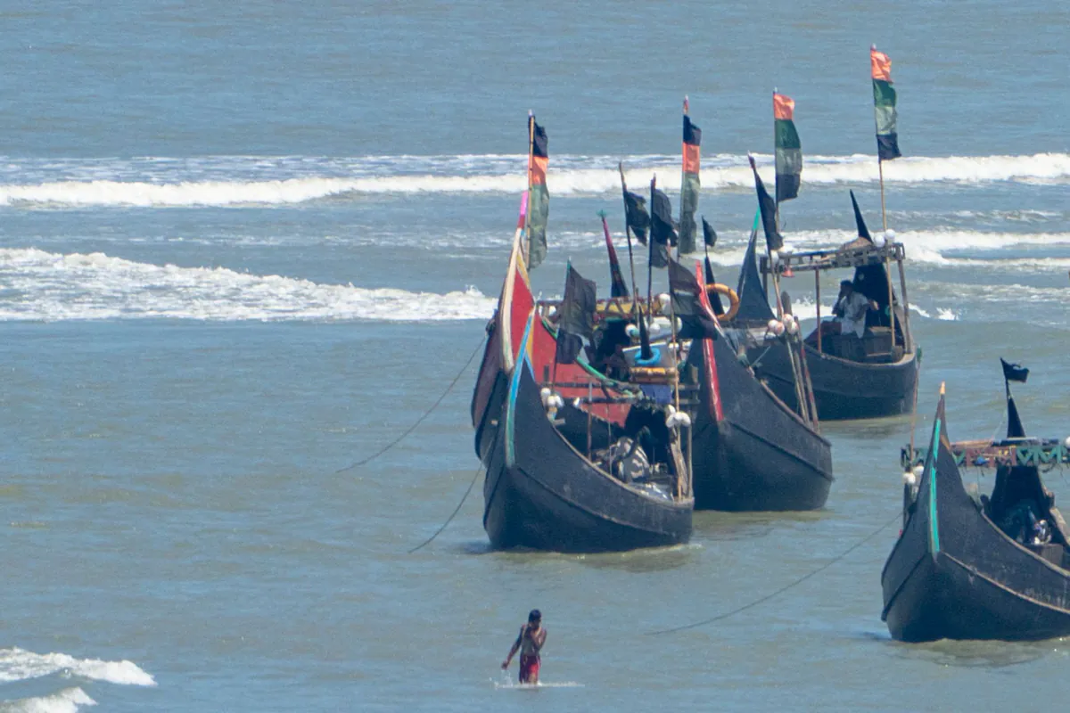 Wooden fishing boats with tall flags anchored in shallow water near the shore, with surf behind
