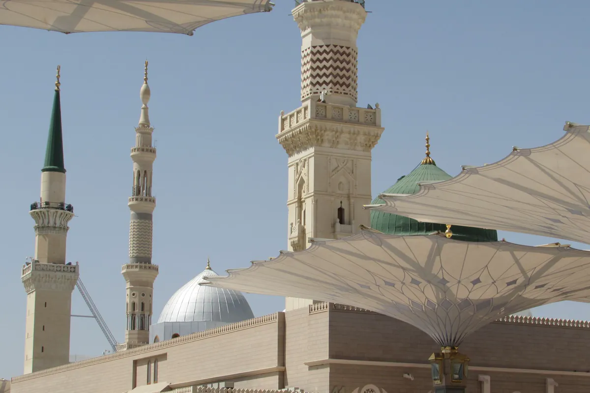 Minarets, a silver dome and the green dome of the Prophet's Mosque behind open shade canopies