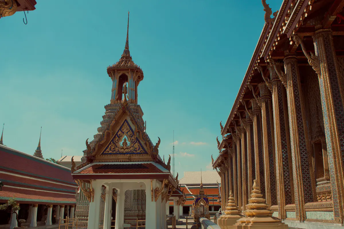 A bell tower with a gilded gable and a row of gilded, mosaic covered columns at Wat Phra Kaew in Bangkok