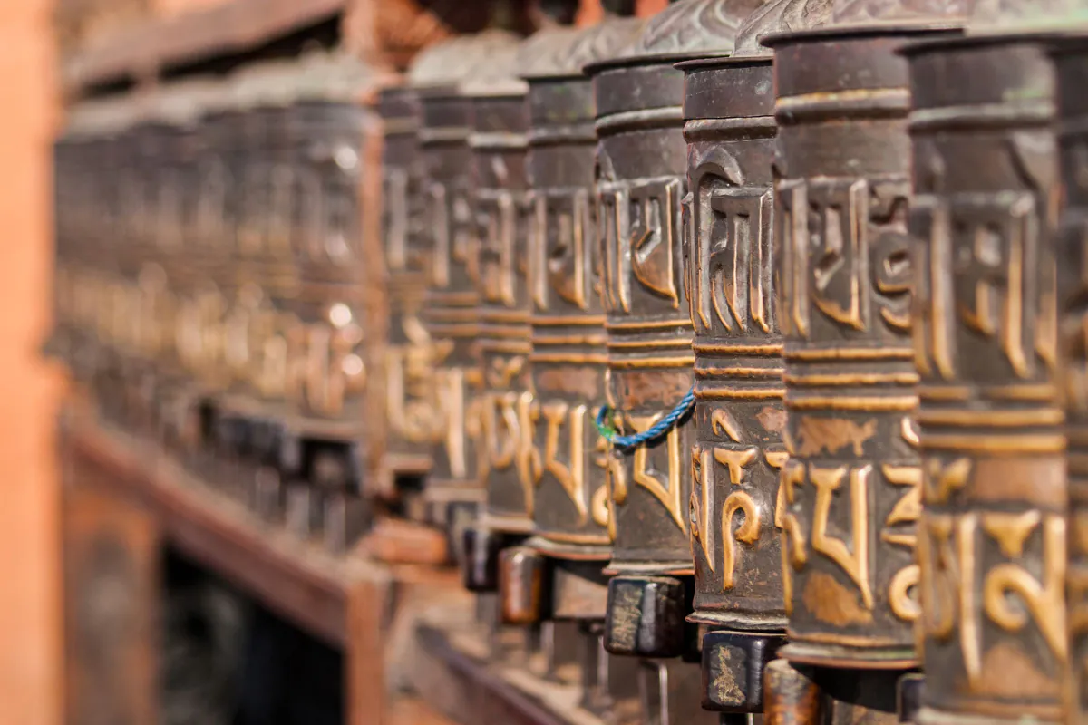 A row of metal prayer wheels embossed with Tibetan script at Swayambhunath in Kathmandu