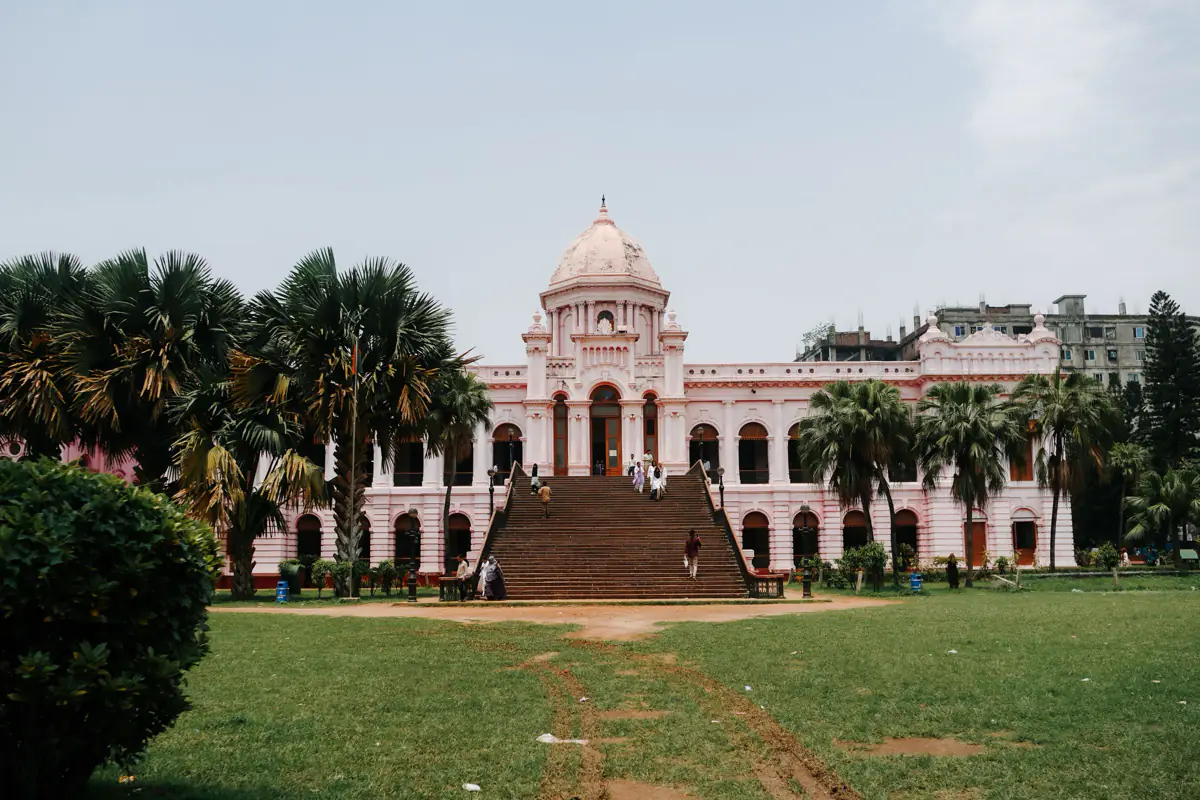 The pink domed Ahsan Manzil palace in Dhaka, with a wide staircase, palm trees and a lawn in front